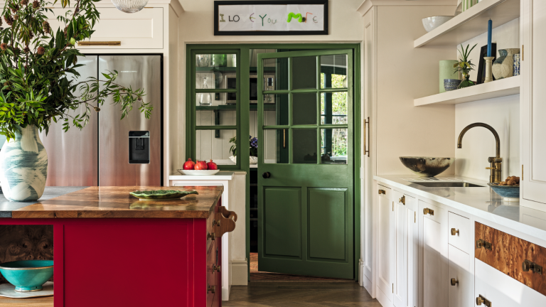 Les portes d’accent sont la réponse de 2026 au mur d’accent obsolète – une façon subtile et sophistiquée d’ajouter de la couleur instantanée a kitchen with a red kitchen island, white cabinets, open shelves, and a green pantry door