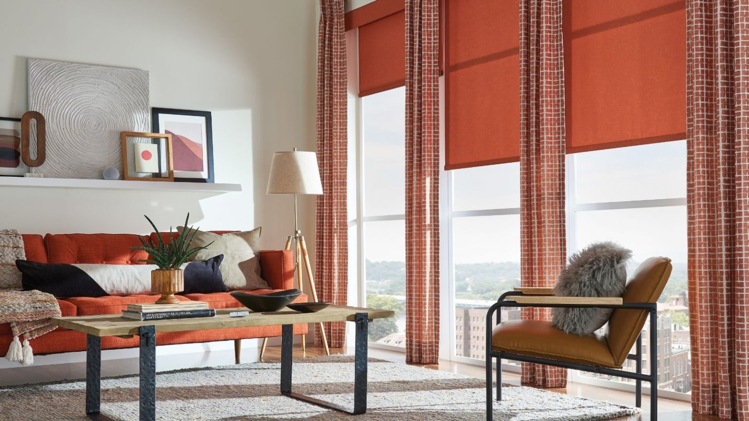 Colorful living room with large red curtains and blinds, red sofa, wooden coofee table and armchair, white rug, and misc art on a floating white shelf.