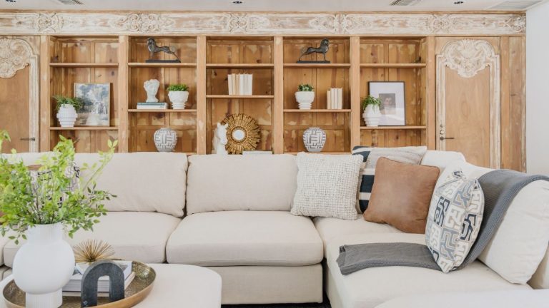 Si vous rembobinez constamment des dialogues télévisés étouffés, cette barre de son Sonos à 199 $ change la donne Living room space with cream L-shaped sofa and coffee table with potted flowers and books, pictured in front of floor-to-ceiling wooden shelves with miscellaneous ornaments and books.