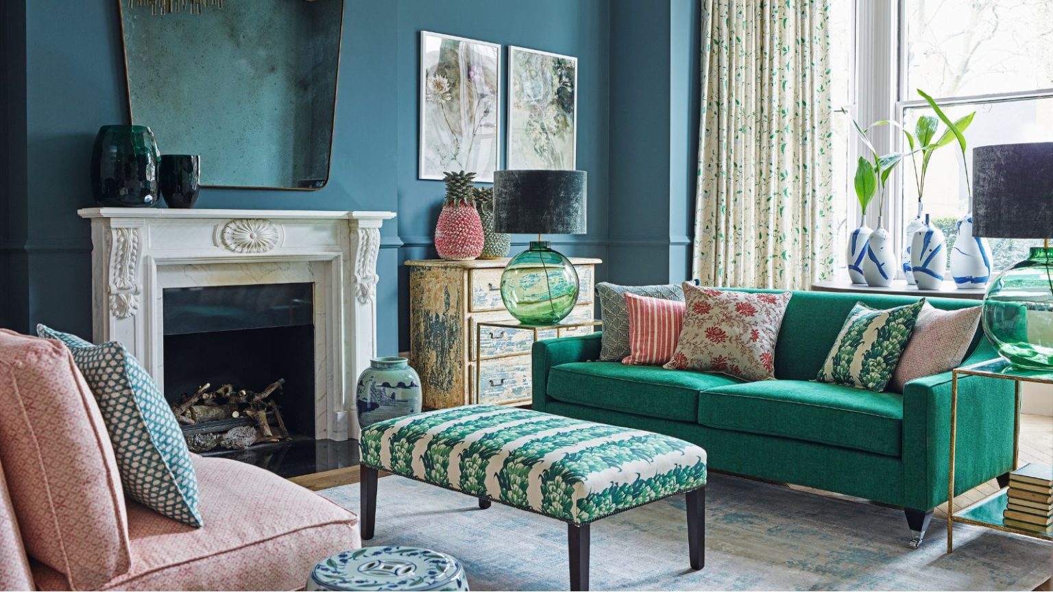 Comment moderniser des meubles anciens pour un look plein de caractère et cohérent Living room with green sofa and assorted cushions, a traditional decorative fireplace and hearth, padded ottoman, ceramic seat, painted furniture piece and teal walls.