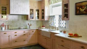 Cette cuisine de caractère est le rêve de tout hôte : c’est le mélange parfait de style et de fonctionnalité et elle est « pleine de solutions de rangement sournoises » A cozy kitchen with pale pink cabinets, warm white wall tiles and white countertops.