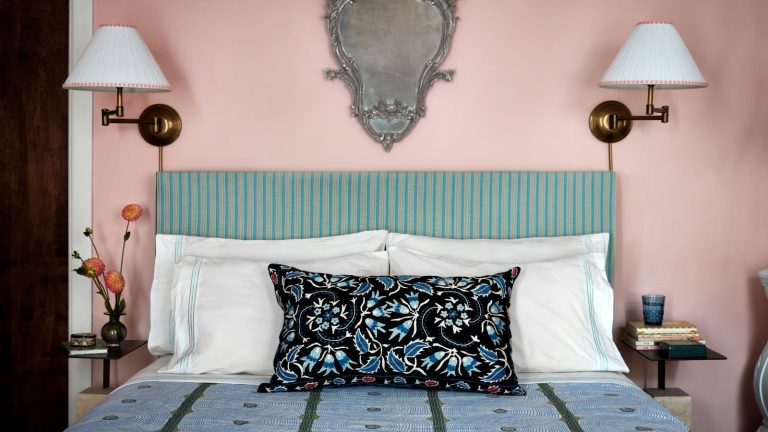 Le « test de seuil » sans culpabilité m’a aidé à désencombrer facilement mon placard d’hiver bien rempli en 5 minutes Blush pink painted bedroom with vintage-looking patterned blue bedding, striped green and cream headboard with paired brass wall lamps and an ornate wall mirror