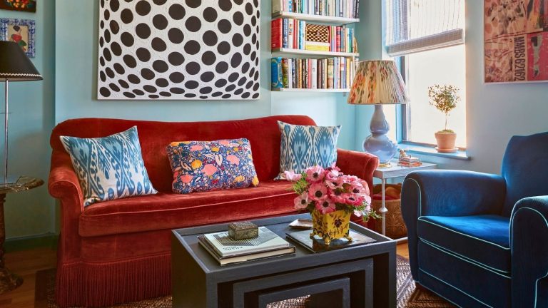 J’ai arrêté de régler le thermostat pendant les vagues de froid – Les experts en CVC disent que le chauffage de panique peut vous coûter plus cher Small and cozy eclectic colorful living room with alcove shelving filled with books, orange and blue velvet sofas, and large black and white geometric artwork on the wall. There is a bright window and a coffee table with books and a vase of flowers
