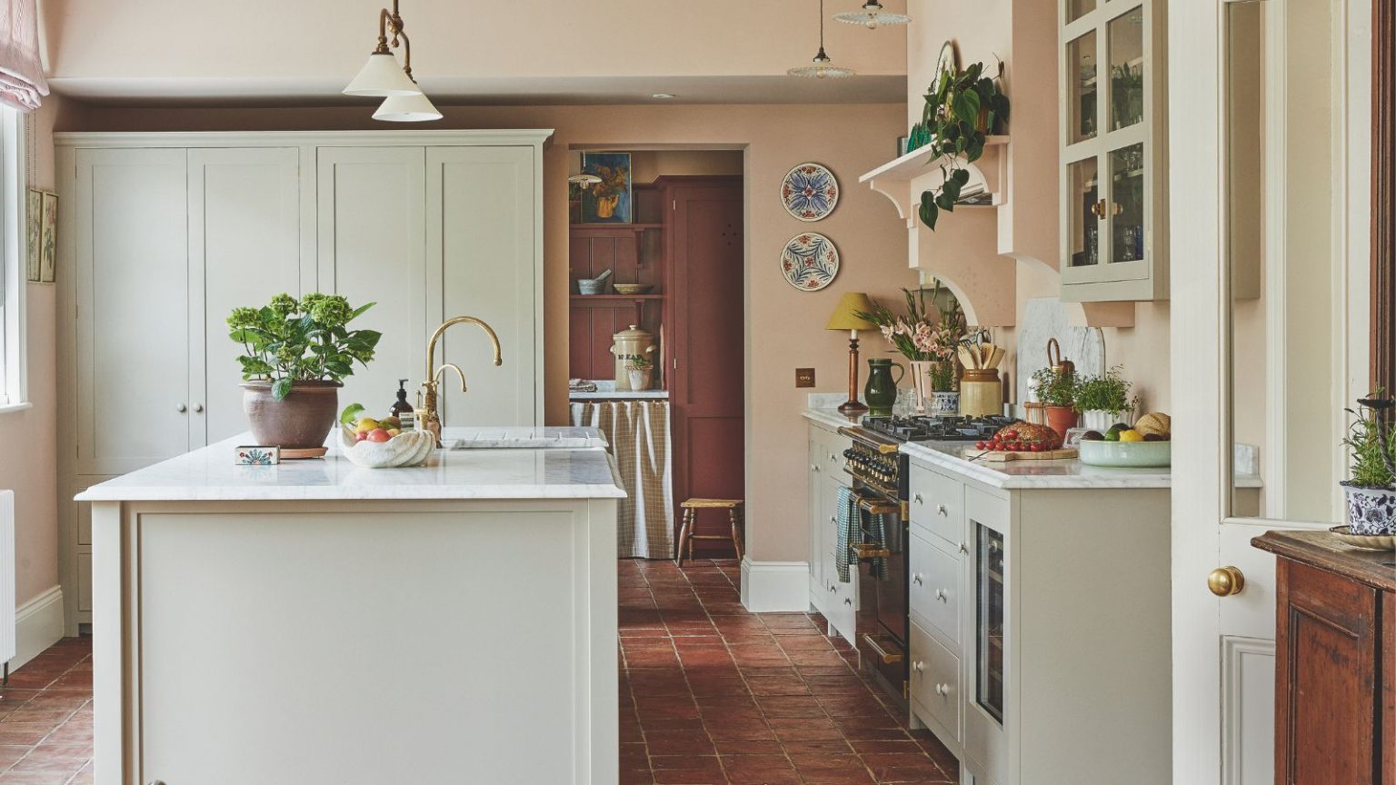 4 couleurs de cuisine qui pourraient dévaluer votre maison – et les teintes les plus intemporelles recommandées par les designers A rustic country style kitchen with light painted cabinets and island, and white countertops. Pink painted walls.