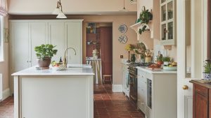 4 couleurs de cuisine qui pourraient dévaluer votre maison – et les teintes les plus intemporelles recommandées par les designers A rustic country style kitchen with light painted cabinets and island, and white countertops. Pink painted walls.