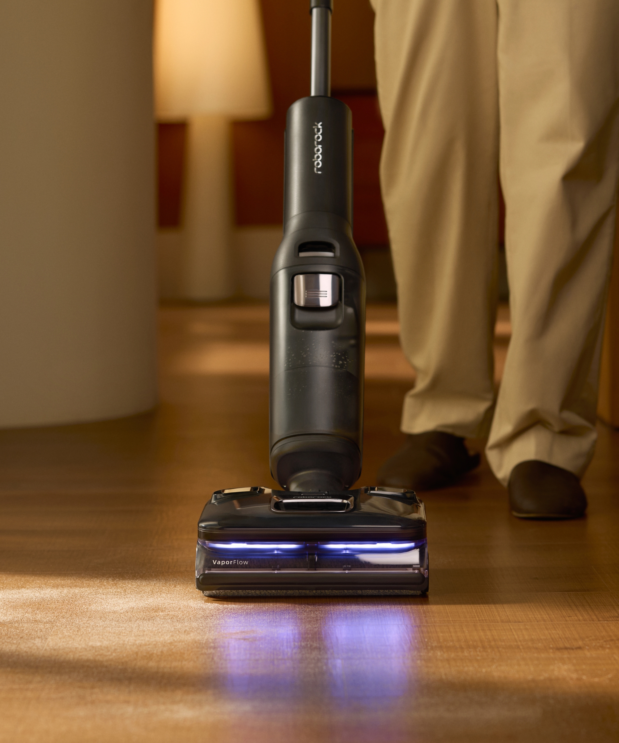 Aspirateur Roborock F25 Ultra sur un parquet en bois avec les jambes de la personne photographiées derrière.