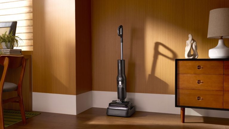 Le Roborock F25 Ultra combine vapeur et eau chaude pour un nettoyage des sols surpuissant Roborock F25 Ultra vacuum-mop on charging base in brown room, pictured between wooden drawers and chair.