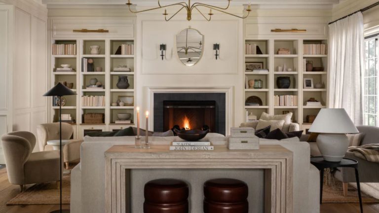 La symétrie est-elle démodée ? Les designers révèlent la formule d’aménagement du salon qui brise les règles et qui va redéfinir la façon dont nous décorons en 2026 neutral living room designed by mcgee and co with lit fire, symmetrical alcove bookshelves, a neutral floating couch with travertine table and little stools