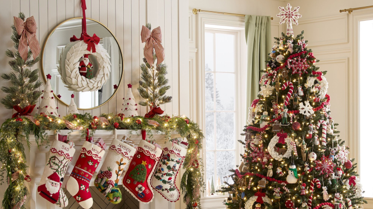 a Christmas display with a mantel and hanging stockings, garland, decorative trees on top of the mantel, a wreath, and a Christmas tree to the right decorated for Christmas