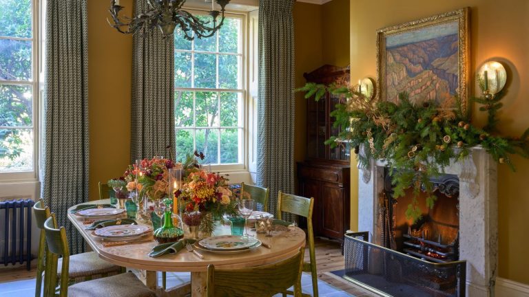 Yellow dining room decorated for Christmas with a wooden table and green chairs and green curtains at the window