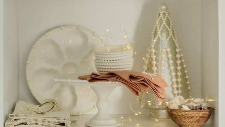 La tendance des décorations de Noël en perles d’Anthropologie est le look le plus chic de la saison – et cette cime d’arbre est la pièce incontournable pour une élégance sans effort. Shelf with pearl side plats, nut bowls, oyster plate and peach pink napkins, plus a glass and pearl Christmas tree ornament