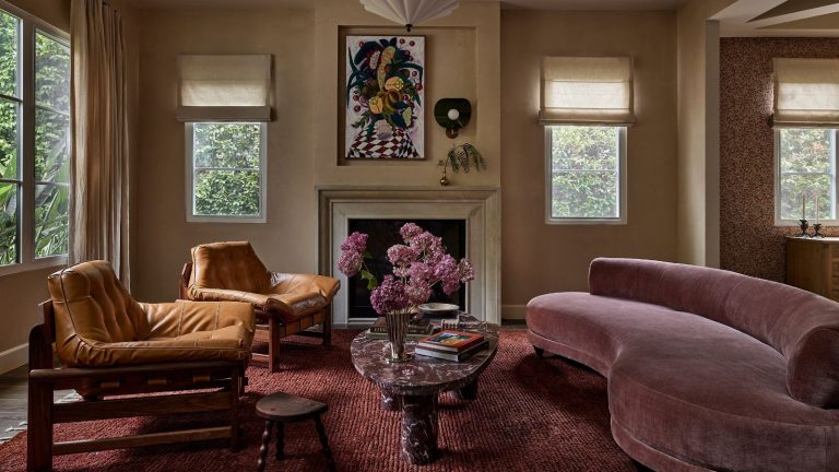 Le mauve est la couleur inattendue que les designers veulent voir davantage en 2026 – Voici comment utiliser avec goût cette couleur codée dans les années 80 A modern living room with neutral walls, a fireplace, a plum-colored rug and a mauve curved sofa.