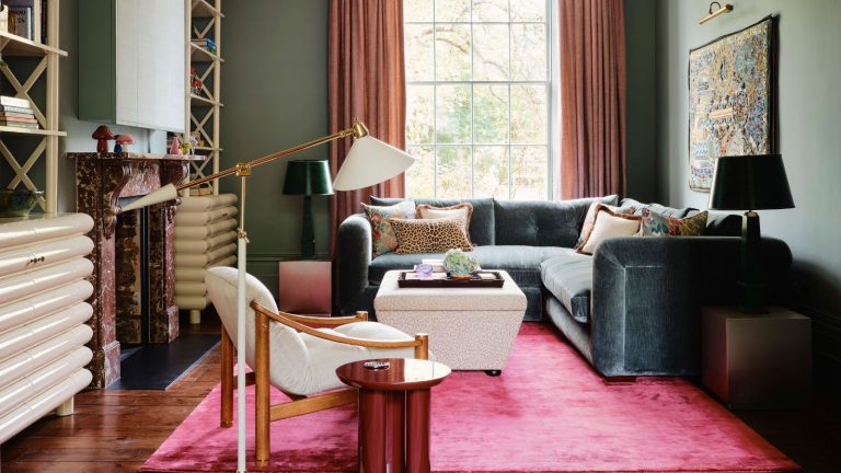L’astuce de zonage simple sur laquelle s’appuient les concepteurs pour rendre le salon de toute taille plus chaleureux, plus intime et plus conversationnel earthy green living room with a large window, vibrant pink deep pile rug with a large green corner couch, small ottoman and a red marble fireplace