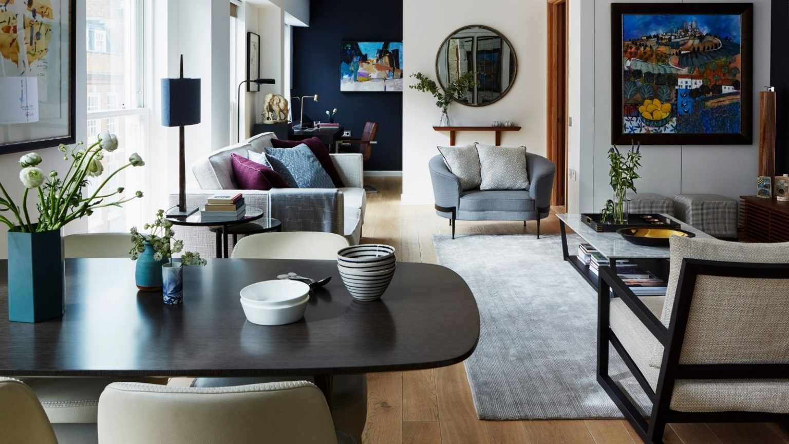 Vous payez toujours trop cher pour chauffer votre maison ? Les experts recommandent ce thermostat intelligent à 59 $ pour réduire les factures An eclectic open plan living and dining room, with a large black dining table in the foreground, various mismatched sofas and chairs with colorful cushions, and a large grey rug to the right with a large coffee table. The walls are white and dark blue, with mirrors, artwork and shelves hung up, and to the right is a large window that's filling the room with light.