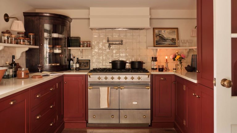 A kitchen with red lower cabinets, a stainless steel double stove, and white back splash tiles.