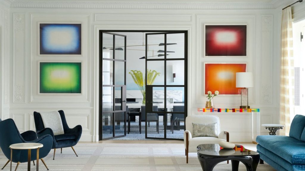 A modern classic living room with navy velvet chairs, colorful abstract art, and black-framed glass doors