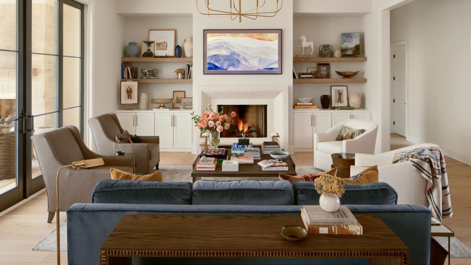 Les concepteurs de styles de sièges inattendus appellent leur « arme secrète » pour un salon plus social cette saison d’accueil neutral living room with a fireplace, built in cupboard and shelves in the alcoves, a blue velvet couch with two bouclé swivel chairs