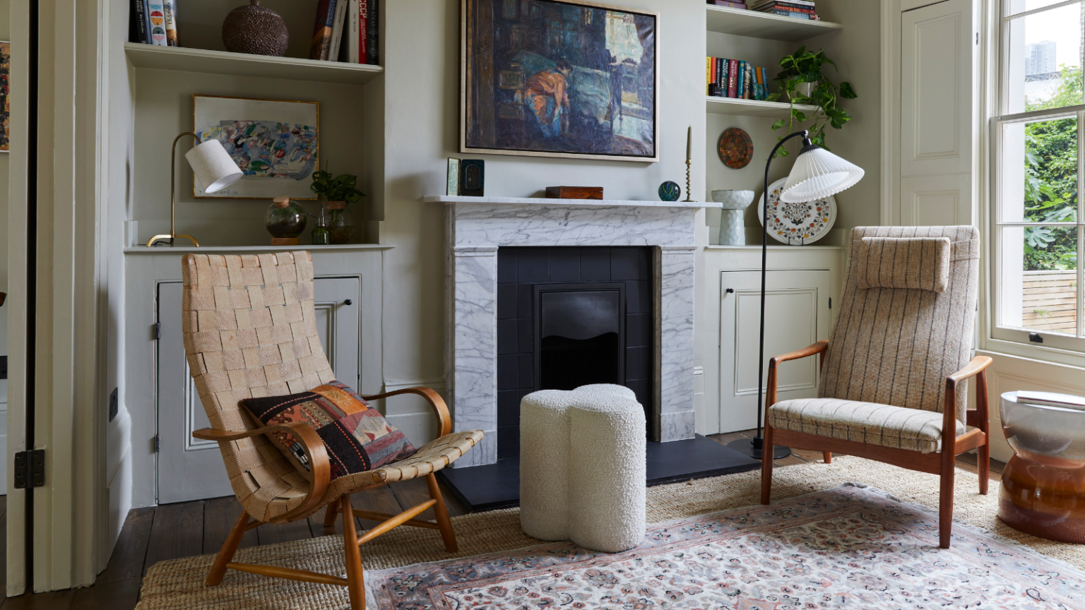 a living room with built-in shelving around a small fireplace, two accent chairs, a boucle stool, and a vintage-inspired persian rug on the ground
