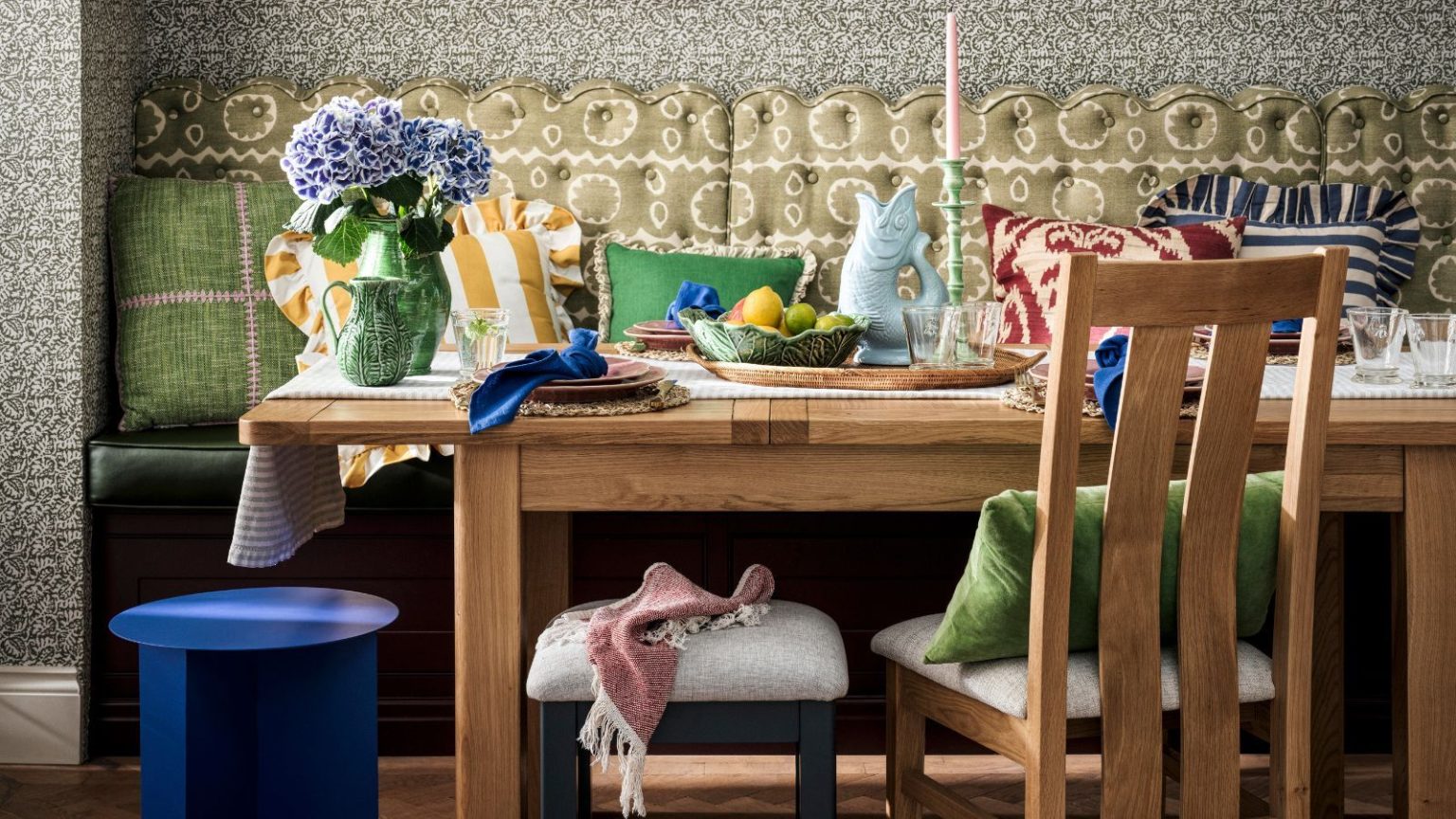 Submergé par les tendances de la nouvelle saison ? Du Cottagecore confortable à une version plus douce du minimalisme, voici les looks AW25 à connaître banquette seat with a scalloped fabric back rest with paisley print, oak table decorated with a cottagecore style and pillows with a small blue stool