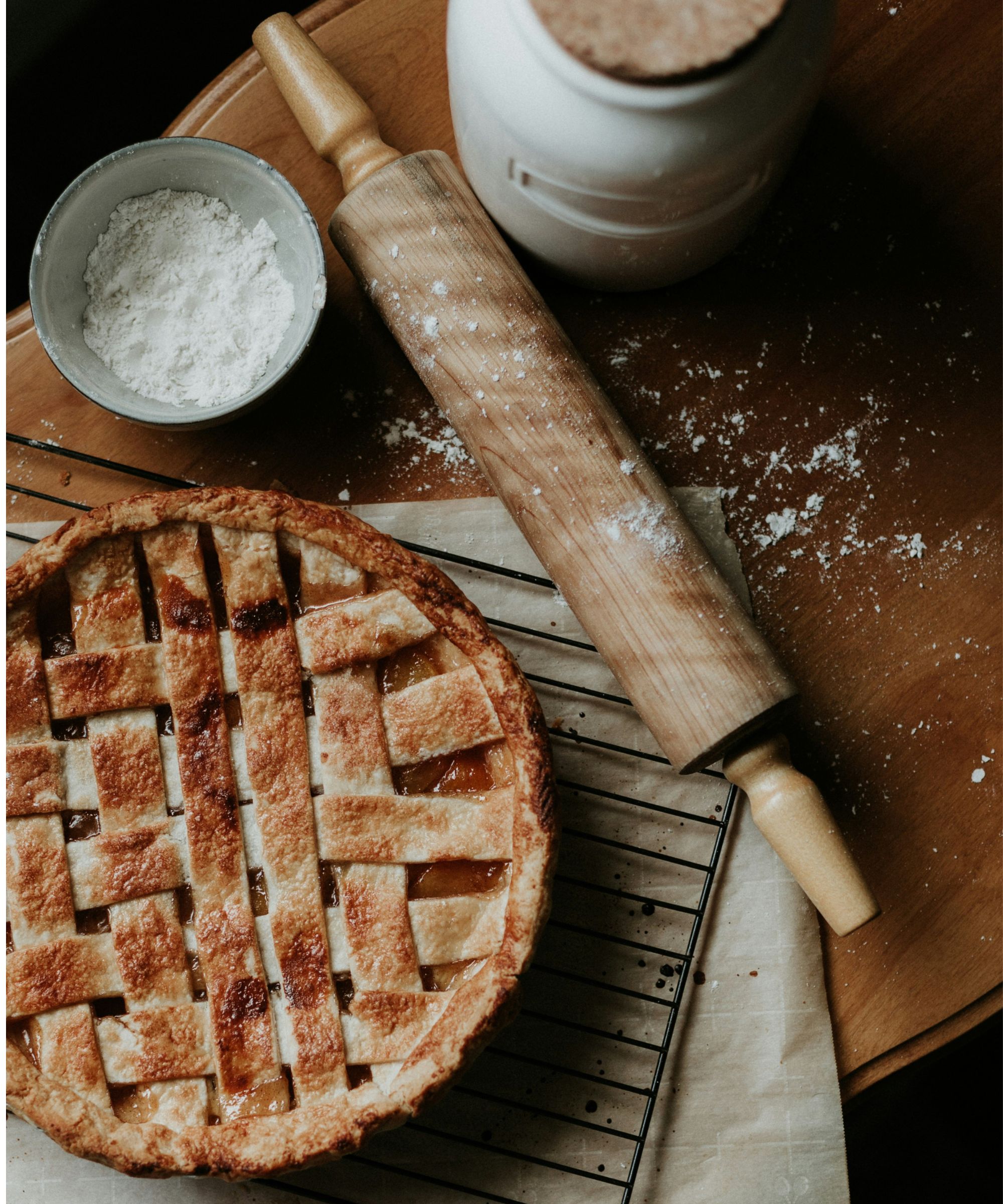 Tarte sucrée sur une grille de refroidissement à côté du rouleau à pâtisserie et du bol de farine