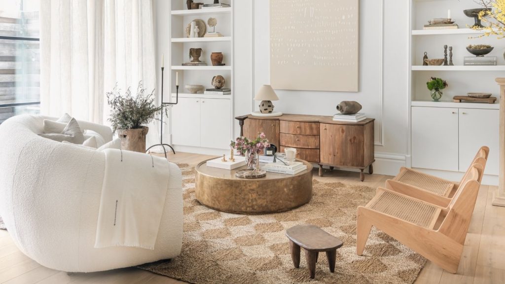 A calm white living room with a white sofa and two wooden armchairs. On a woven rattan rug, with light wooden flooring.