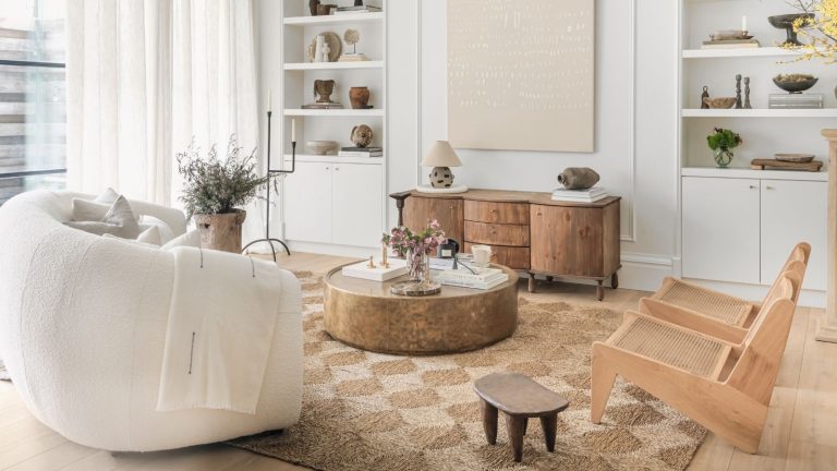 A calm white living room with a white sofa and two wooden armchairs. On a woven rattan rug, with light wooden flooring.