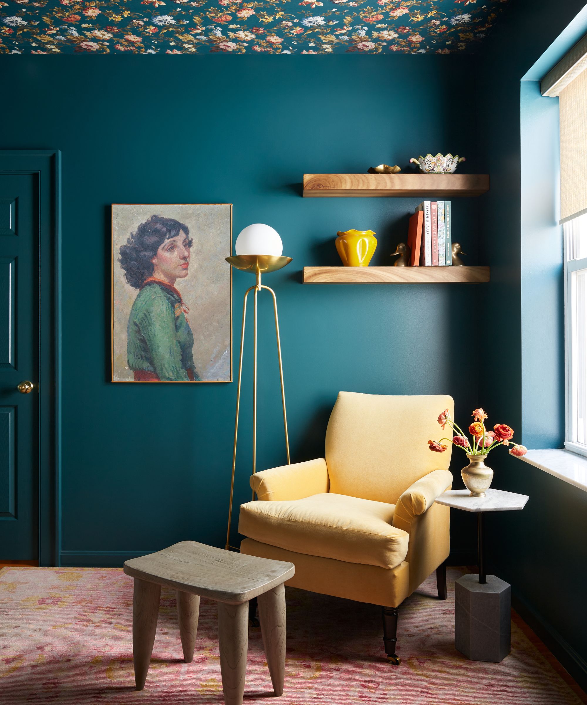 Une pièce bleu foncé avec du papier peint à fleurs au plafond, un tapis rose poussiéreux et une chaise d'appoint ocre.