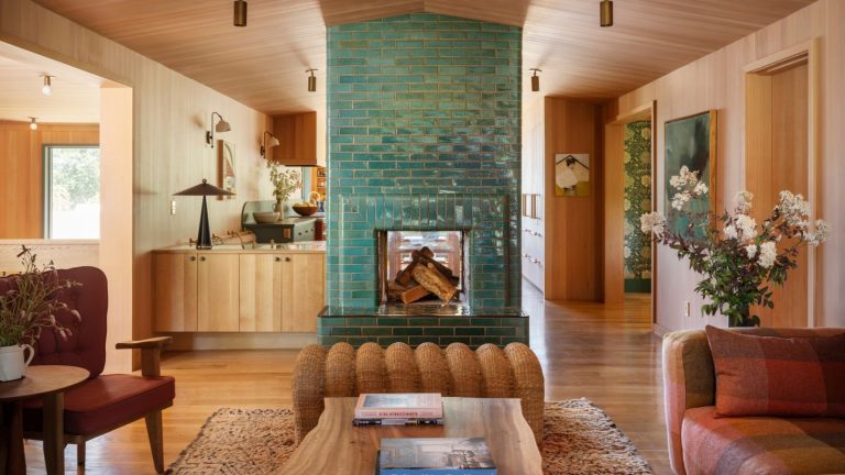 La sarcelle est le bijou que les créateurs utilisent pour rendre les maisons plus luxueuses – et ce sont les trois endroits clés où ils l’utilisent. An open-plan living room with a teal brick fireplace, wooden walls, ceiling and kitchen cabinets.