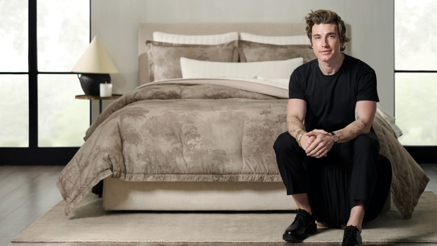 Jeremiah Brent vient de lancer sa première collection de literie chez Target – Cette ligne intemporelle a l’air beaucoup plus chère qu’elle ne l’est Jeremiah Brent sitting at the foot of a bed with a watercolor duvet color on the bed