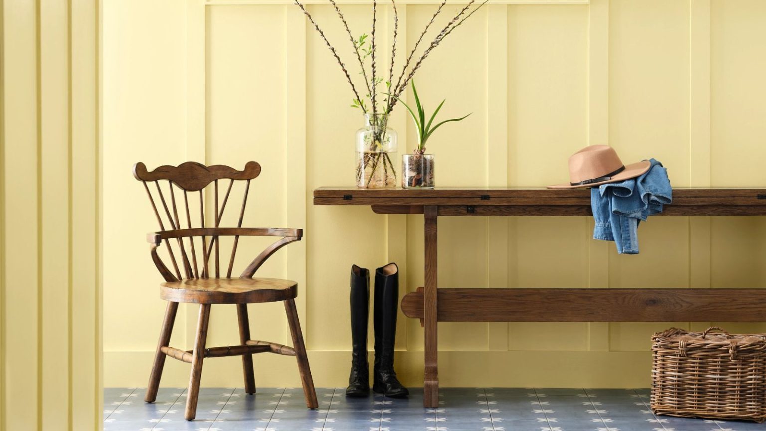 Les couleurs de peinture les plus heureuses de Sherwin-Williams rehausseront instantanément l’ambiance de votre maison en 2026 – ce sont les 4 avec lesquelles commencer à décorer a panelled entryway painted in a sunshine yellow with a rustic wooden bench, vintage wooden chair, boots, and vases of foliage