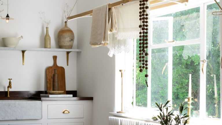 Faut-il faire la lessive pendant une tempête hivernale ? Les plombiers préviennent que cela peut geler les tuyaux et provoquer des inondations – faites ceci à la place White laundry and utility room with a wooden ceiling rack. There is open shelving with stone vases and wooden cutting board in view