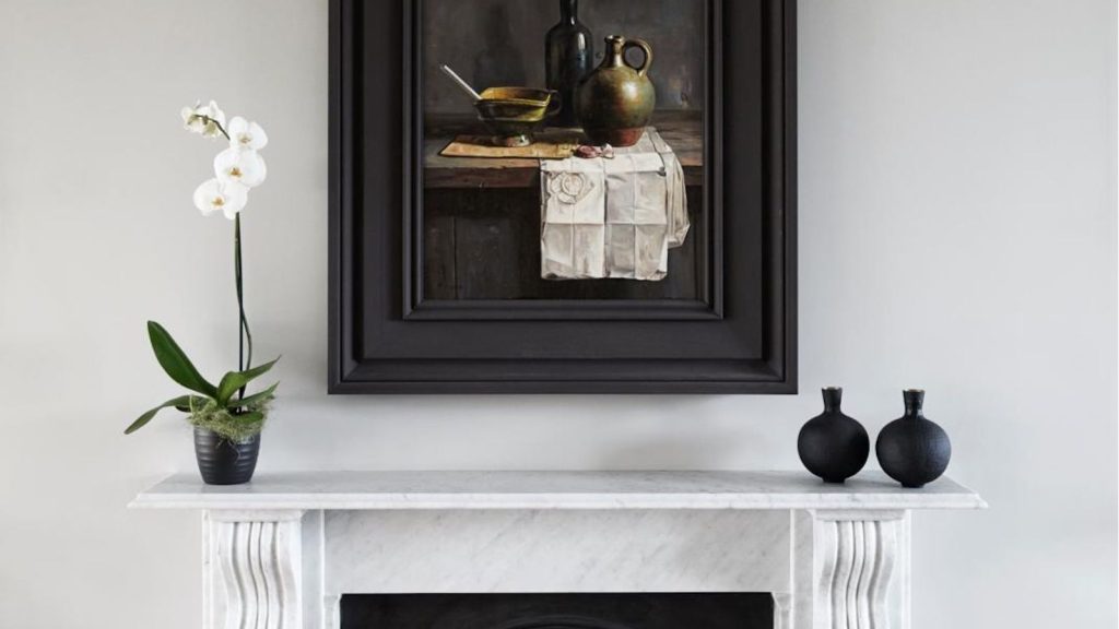 White orchid in bloom in a black pot on a marble mantlepiece, with black bud vases on the other end and black-framed still-life art on the wall