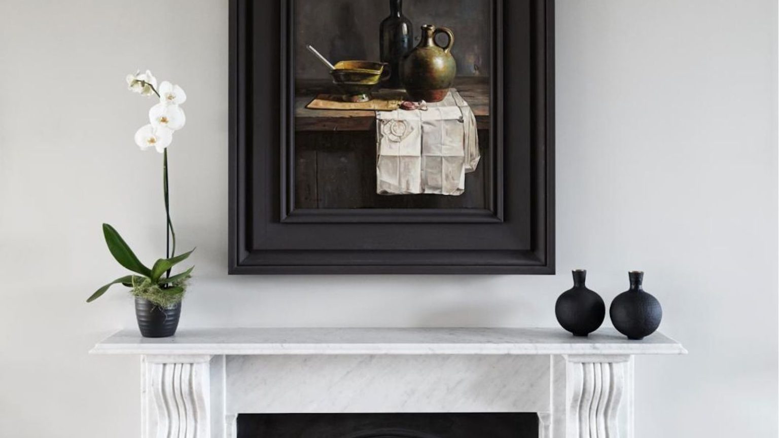 Faire refleurir une orchidée est plus facile que vous ne le pensez – 5 façons approuvées par des experts de déclencher des floraisons répétées spectaculaires White orchid in bloom in a black pot on a marble mantlepiece, with black bud vases on the other end and black-framed still-life art on the wall