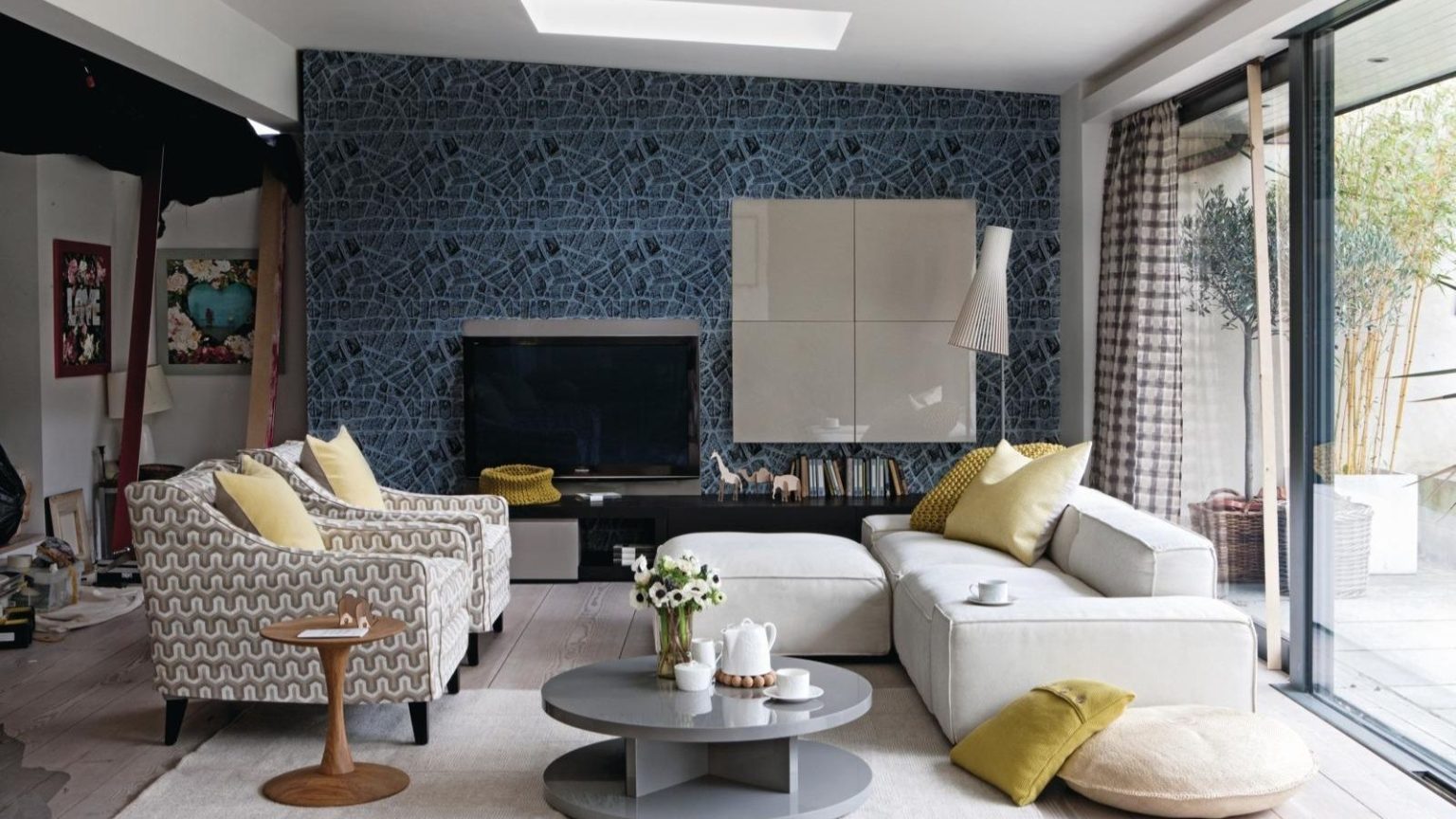 Votre téléviseur 4K mérite mieux qu’un son plat – Améliorez votre divertissement à domicile avec une barre de son Dolby Atmos en plein essor pour seulement 175 $ Gray living room, grey graphic patterned wallpaper, white fabric sofa with matching footstool, armchairs upholstered in hexagonal patterned fabric , yellow scatter cushions, grey veneer coffee table, lacquer Boiserie TV panel, lacquer four cube wall unit, sliding patio doors