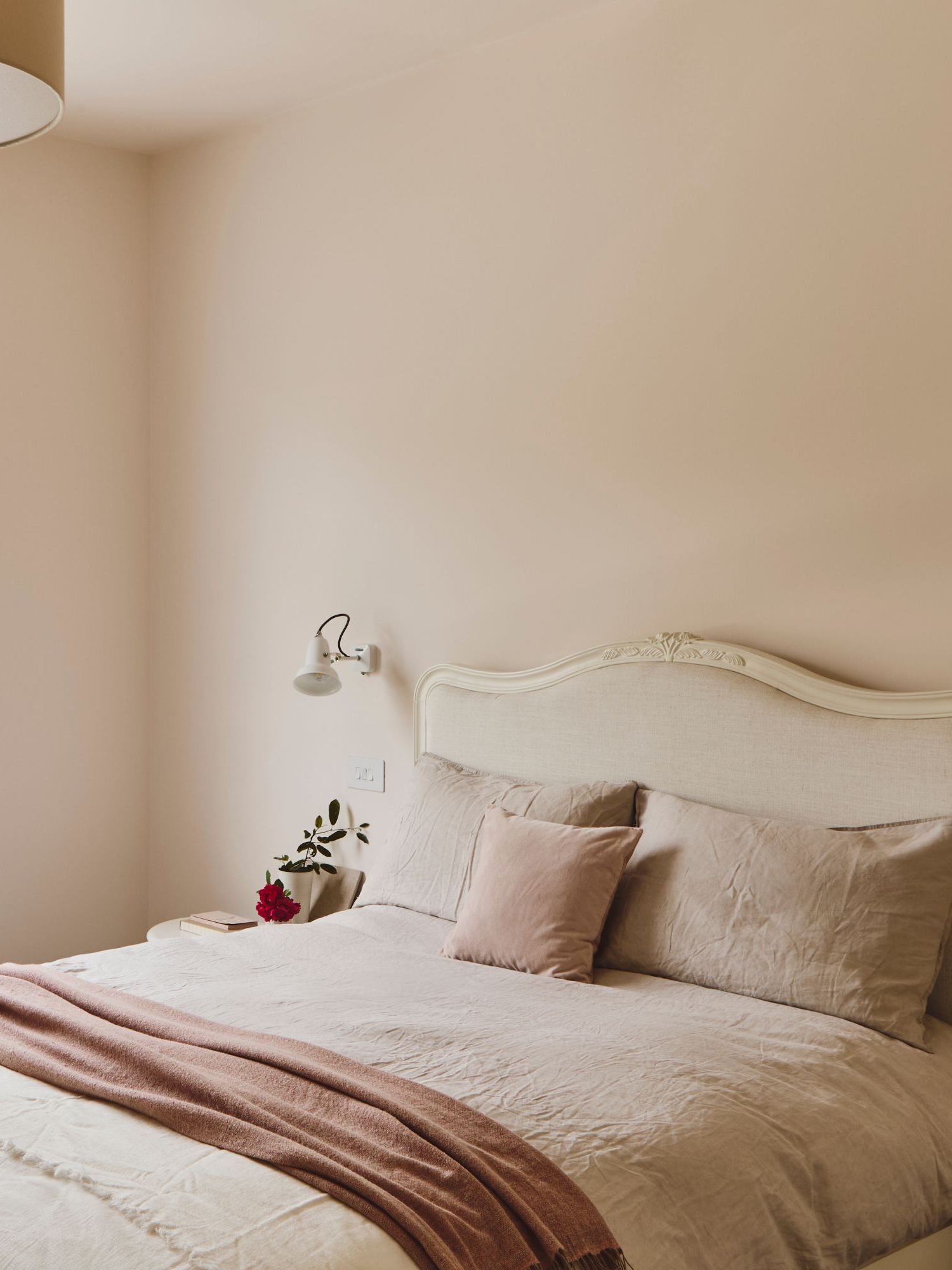 Une chambre avec des murs rose clair, une literie en lin neutre et une grande fenêtre avec un store romain.