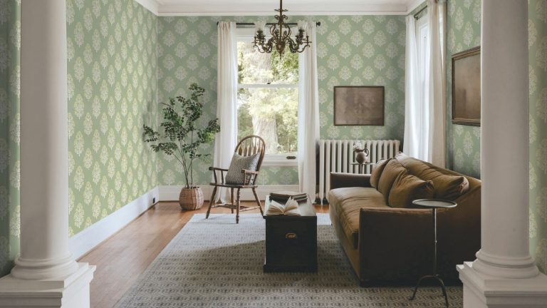 Cozy small living room with hard floors and radiator in view. There is a sofa, ottoman coffee table, and patterned sage wallpaper