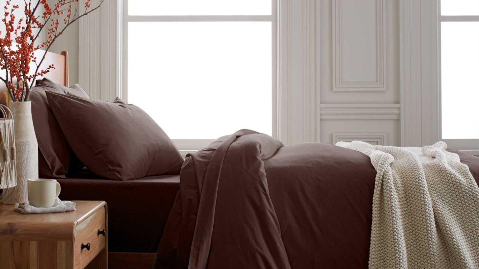 J’achète ces feuilles de coings pour tous ceux que je connais ce Noël – Faites-moi confiance, ces feuilles conviennent à tous, et il y a une rare réduction de 25 % en ce moment Dark brown bedding on a wooden bed with a wooden bedside table decorated with a vase of orange berries