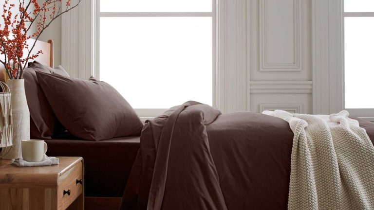 J’achète ces feuilles de coings pour tous ceux que je connais ce Noël – Faites-moi confiance, ces feuilles conviennent à tous, et il y a une rare réduction de 25 % en ce moment Dark brown bedding on a wooden bed with a wooden bedside table decorated with a vase of orange berries
