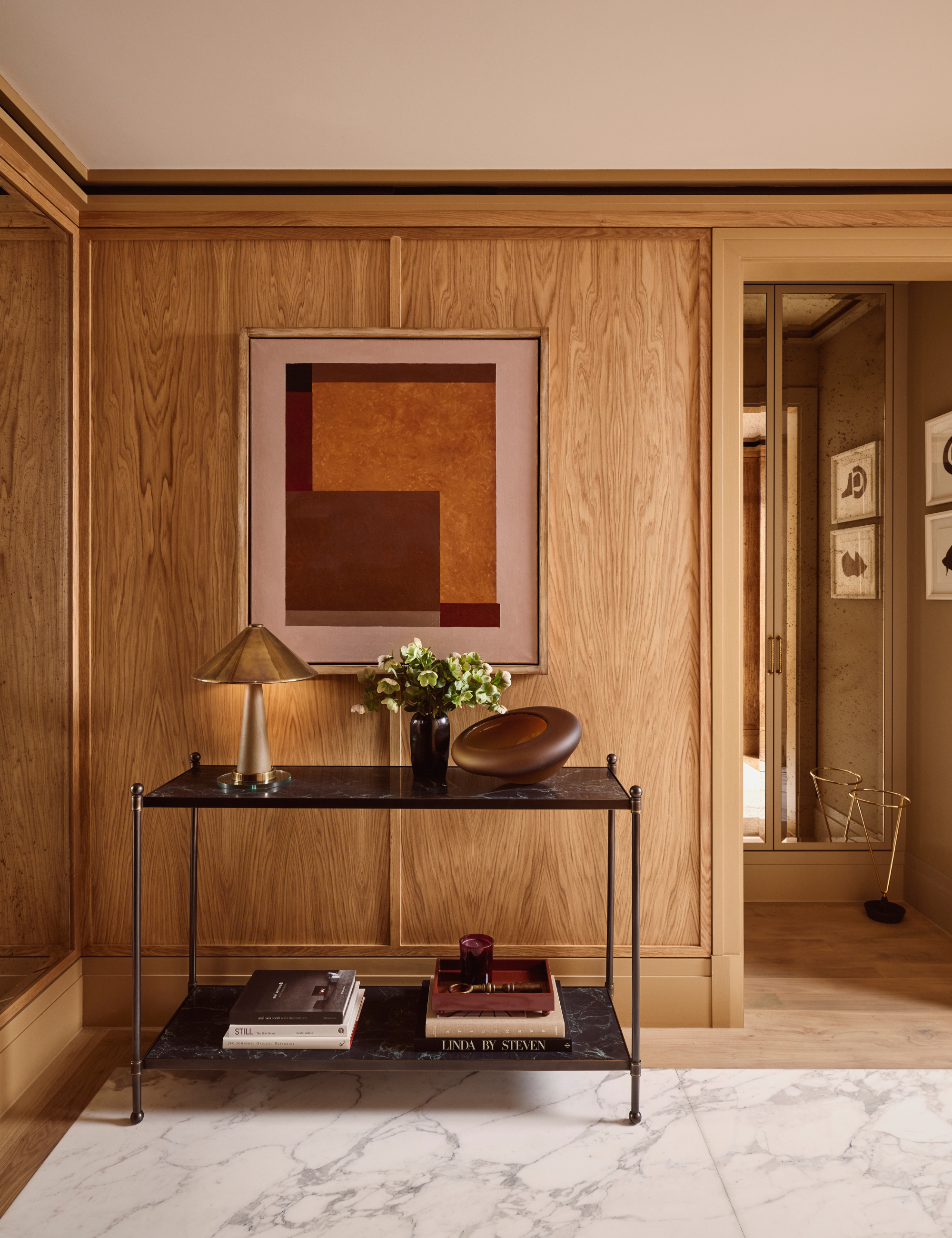 Zone d'entrée lambrissée en bois comprenant une table en métal noir à deux niveaux contenant divers objets collectés