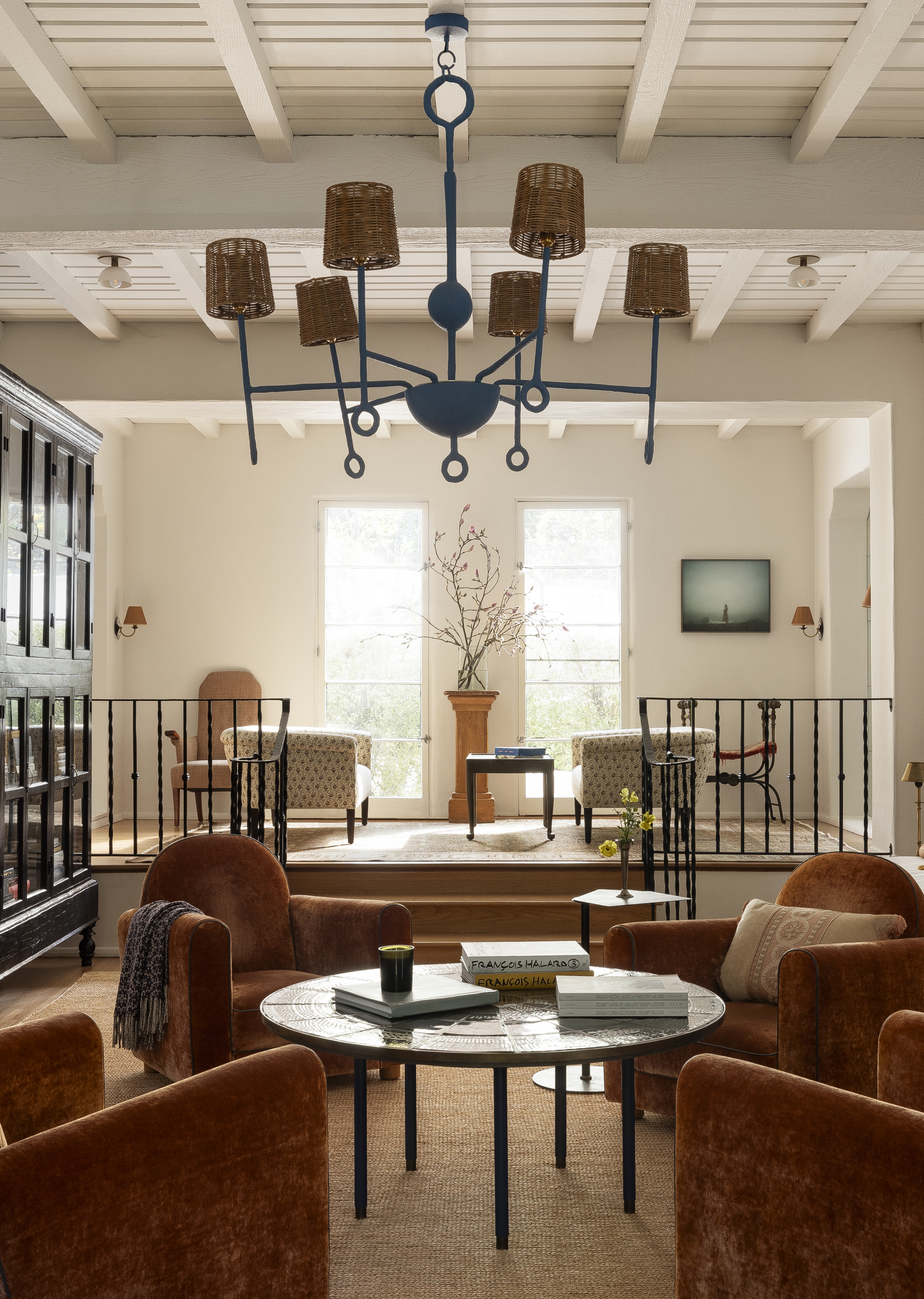 Sous un luminaire peint en bleu, quatre fauteuils club en velours entourent une table basse ronde dans un salon de Los Feliz.