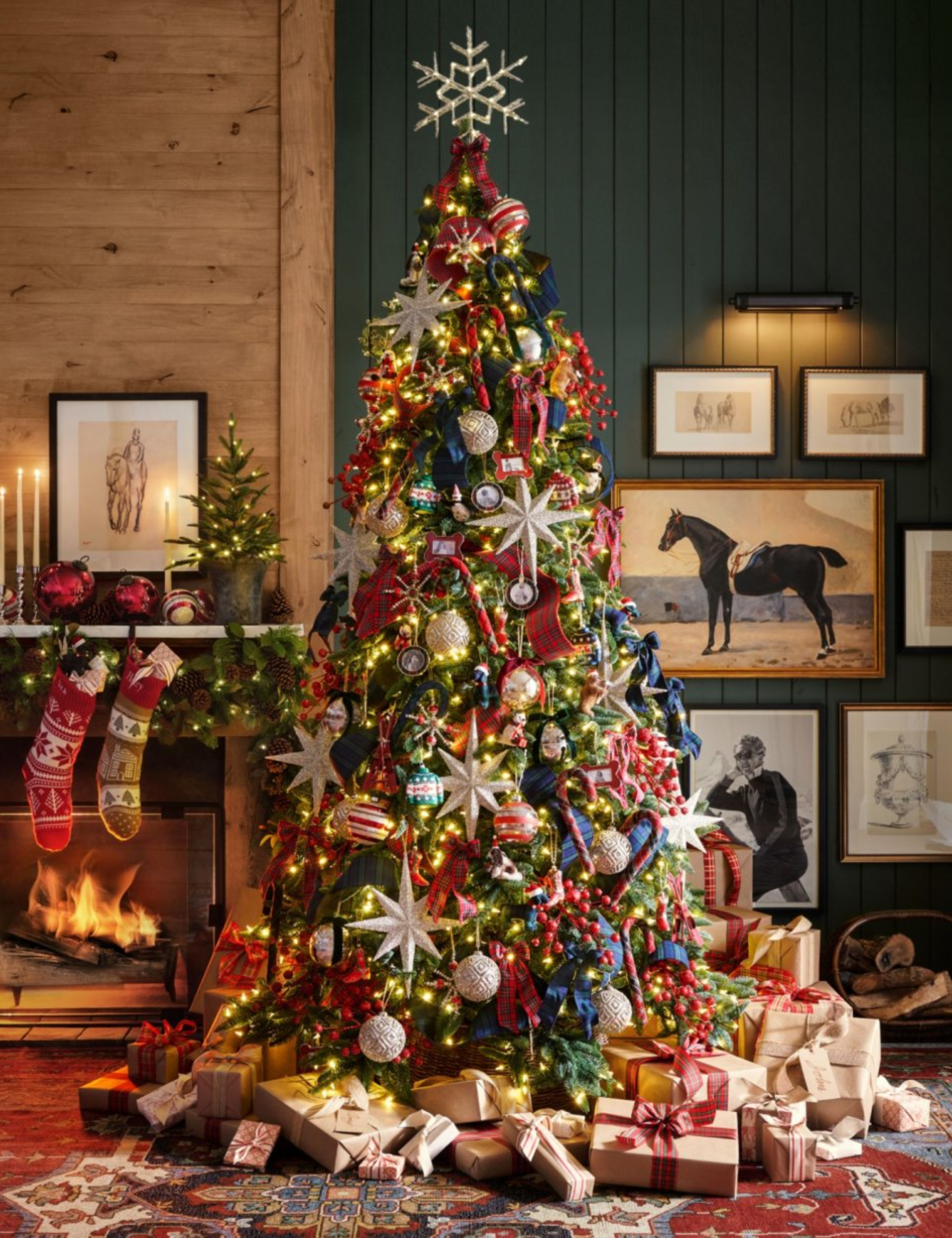 Salon de Noël inspiré de Ralph Lauren avec un sapin de Noël lumineux et très décoratif, des bas en tricot et des œuvres d'art murales équestres.
