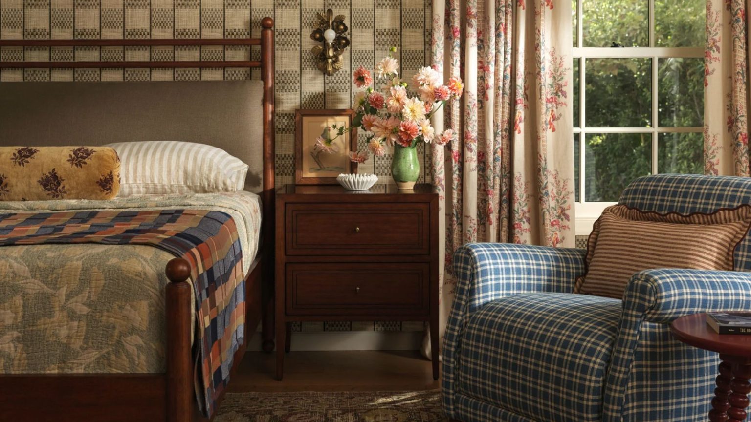 De manière inattendue, ce style d’éclairage autrefois démodé est le seul changement que je fais pour rafraîchir ma chambre confortable de chalet en 2026. cozy cottage bedroom designed by Heidi Caillier for Lulu and Georgia with checked wallpaper, floral curtains, plaid chair and wooden bed and nightstand