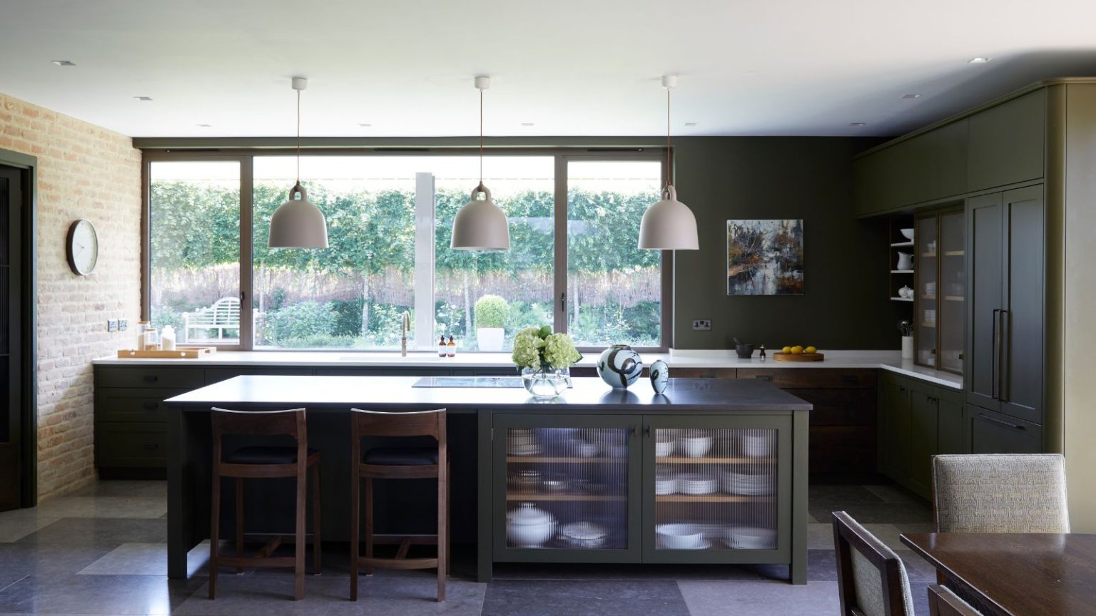 Déplacez-vous vers un luxe silencieux, la palette Loud Luxury de Sherwin-Williams prouve que des couleurs riches et dramatiques sont ce dont nous avons tous envie en 2026 Kitchen with olive green cabinets and island, three pendant lights, tiled floor