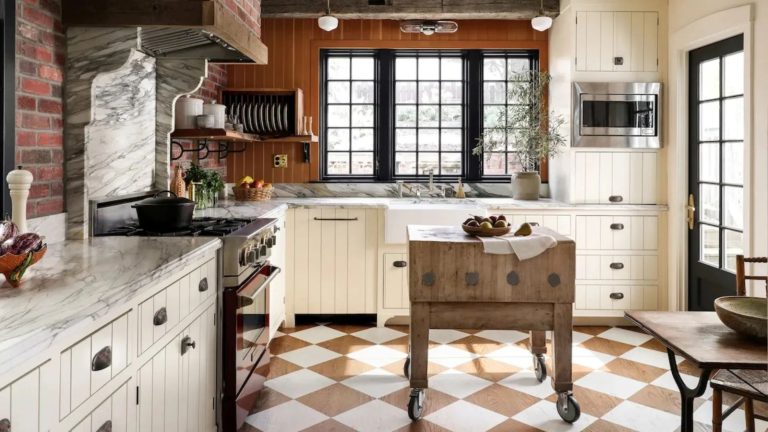 C’est la pièce sous-estimée qui manque à votre cuisine si vous avez besoin d’ajouter rapidement du stockage supplémentaire et de l’espace de surface – et elle correspond également à une énorme tendance 2026 a country kitchen with painted checkerboard floors, white cabinetry, and a butcher block portable cart at the center