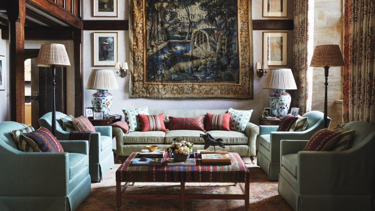 « En cas de doute, ajoutez » – À l’intérieur d’une maison de campagne More is More réinventée avec des couleurs vives et une cuisine inspirée de celle du designer living room of a traditional jacobean home with wooden beams and a large tapestry hung on the wall, styled with artwork, a light green sofa, four tub chairs and a striped upholstered ottoman
