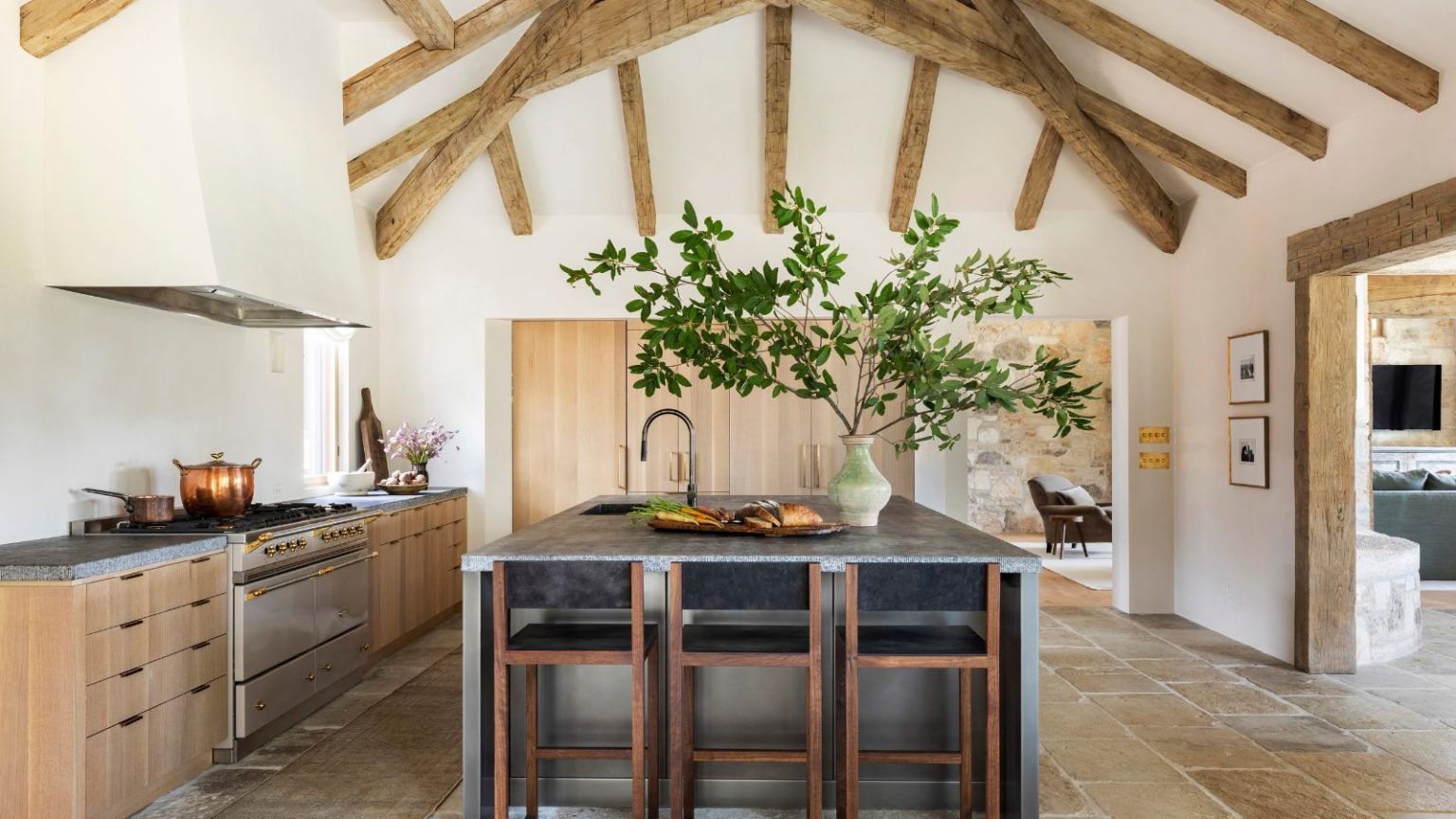 Oubliez tout ce que vous pensez savoir sur la conception de cuisine : ces 4 caractéristiques étaient autrefois des « indispensables », mais maintenant les concepteurs disent de les laisser de côté A large kitchen with tall ceilings featuring wooden beams, wooden cabinetry, gray countertops, a stainless steel island, and no upper cabinets of backsplash for a softer look