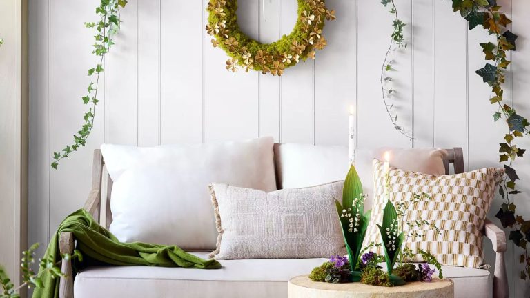J’ai toujours évité la décoration de la Saint-Patrick – mais cette année, la collection chic vert et or de Terrain m’a fait changer d’avis Bright white sunroom featuring a white sofa accented with a green throw blanket and patterned throw pillows. Elsewhere, there is a stone side table holding lily of the valley taper holders and a shamrock wreath hanging overhead