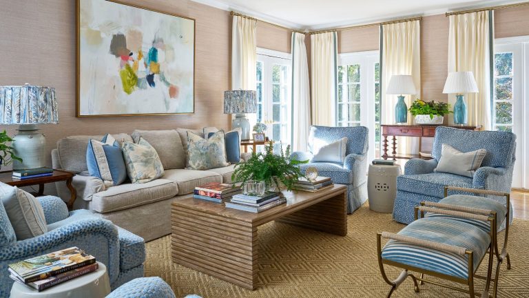 5 erreurs de décoration vintage qui donnent à votre maison un aspect coincé dans le passé – et comment les designers mettent fin à l’effet capsule temporelle Living room with pale pink grasscloth walls, wooden coffee table, blue and cream sofas and armchairs and mahogany tables with large lamps