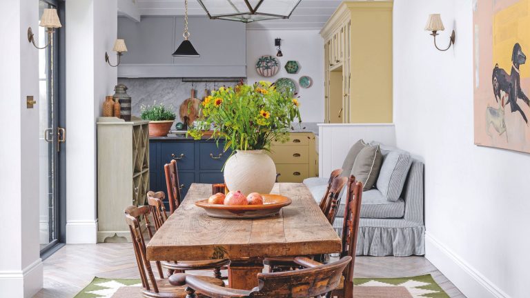 Cette maison de ville de l’ouest de Londres cachait un studio secret – c’est maintenant une cuisine à couper le souffle A bright, airy dining space with a rustic wooden table, antique spindle chairs, and a large glass lantern pendant light hanging from a vaulted white ceiling.