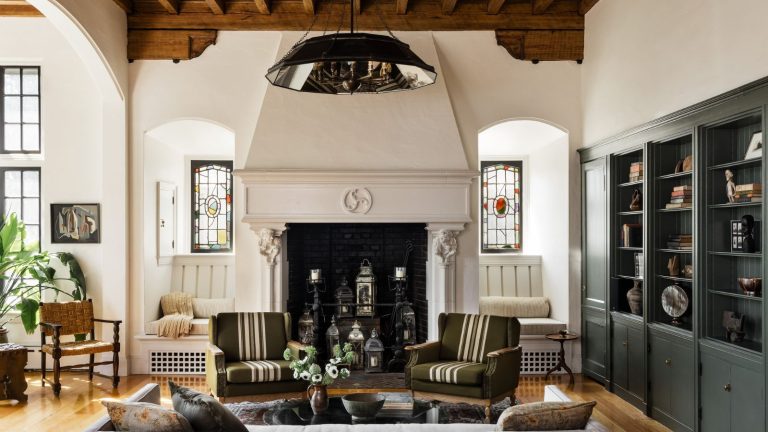 Le « Subwoofer Crawl » est la technique de 2 minutes que les ingénieurs du son utilisent toujours pour un son domestique parfait Textured living room with wooden-beamed ceiling, dark green bookshelves to the right, two striped armchairs, stained glass windows, a hanging lightshade, and wooden floors.